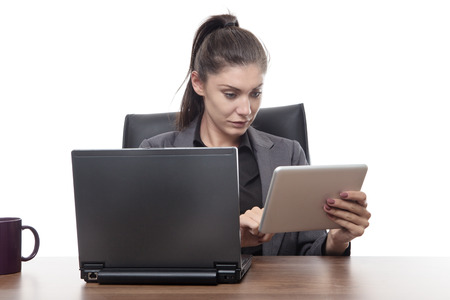 business woman sitting at her desk working on a laptop and tablet computerの写真素材