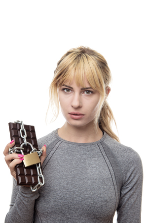 fitness woman holding a chocolate bar locked up in chainsの写真素材