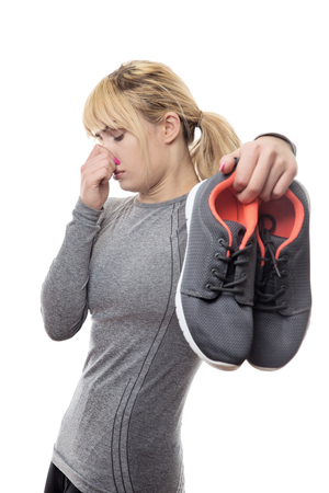 blonde haired woman holding up her smelly gym shoesの写真素材