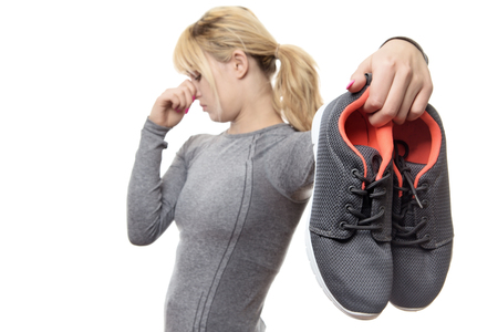 blonde haired woman holding up her smelly gym shoesの写真素材