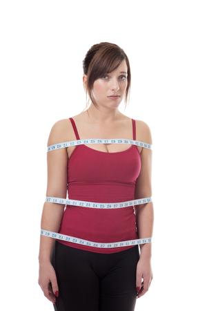 shot in the studio of young fitness woman with a tape measure wrapped around body looking unsureの写真素材