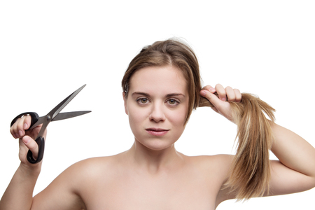 young woman with long hair cutting it of with a pair of scissors having a bad hair dayの写真素材