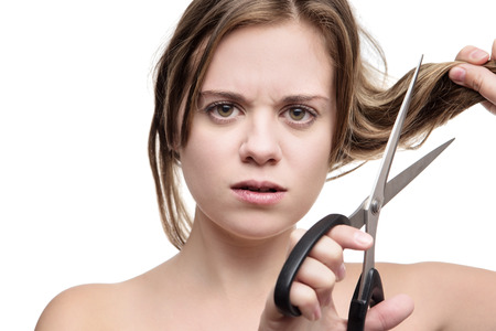 young woman with long hair cutting it of with a pair of scissors having a bad hair dayの写真素材