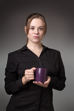 young standing business woman shot in the studio on a grey background holding a cupの写真素材