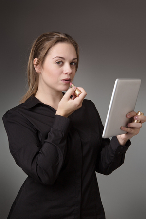 young business woman putting on lipstick using a tablet computer as a mirrorの写真素材