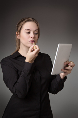 young business woman putting on lipstick using a tablet computer as a mirrorの写真素材