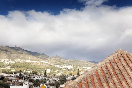 landscape shot looking across the  hoilday city resort of Benalmadena in spain at the montinas with the top of a red tiled roof in the foreground.の写真素材