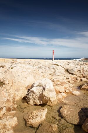 close up of a rocky beach in Qawra Point in Malta with a metal post painted red in the groundの写真素材