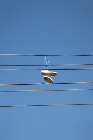 a pair of trainers thrown over a power line, commonly believed  to signal the location of a crack house / drug dealing spot. Can also be the symbol of gang members claiming territory.の写真素材
