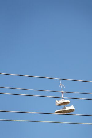 a pair of trainers thrown over a power line, commonly believed  to signal the location of a crack house / drug dealing spot. Can also be the symbol of gang members claiming territory.の写真素材