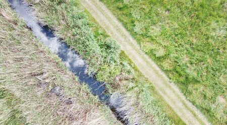 birds eye view of the ground below with a river and pathway running parallel together in the imageの写真素材