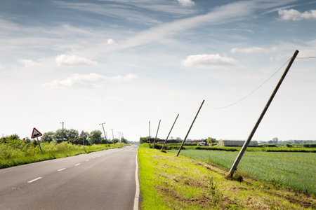 telephone poles leaning over from the wind along a countryside road in england
