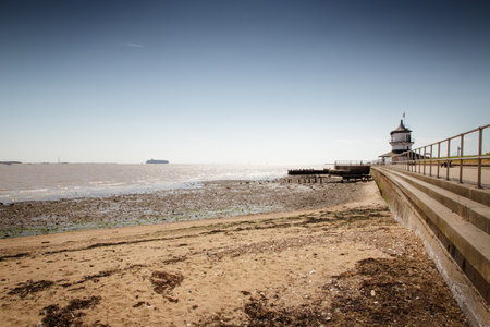 landscape image of the low lighthouse in harwich looking out to sea at a cargo ship coming into port at felixstoweの写真素材