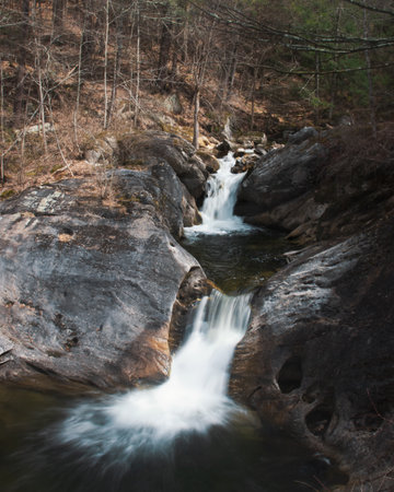 Long exposure photo of a waterfall running off of some rocks. Bright photo with warm tones. Forest. No people in frame.の写真素材