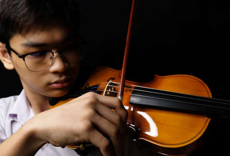 Young Asian man playing violin on dark backgroundの写真素材