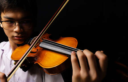 Young Asian man playing violin on dark backgroundの写真素材
