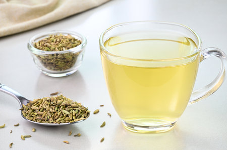 Fennel seed water in a glass cup with fennel seeds in the backgroundの写真素材