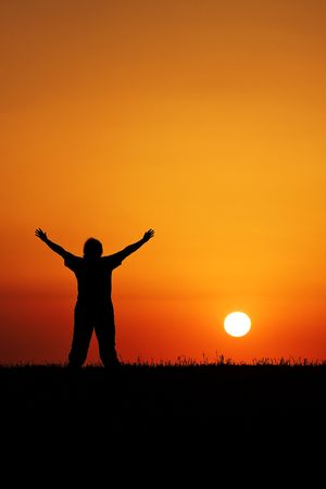 A young person with hands in air in front of beautiful blood red sunsetの写真素材