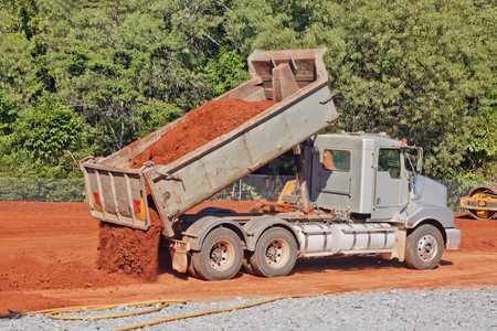 A tip truck is dumping red dirt or soil at a construction siteの写真素材