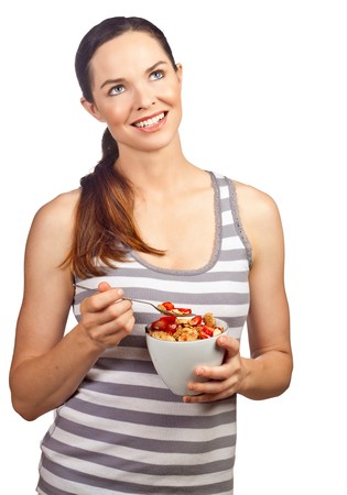Portrait of a beautiful young woman eating a healthy bowl of cereal with strawberries. Isolated over white.の写真素材