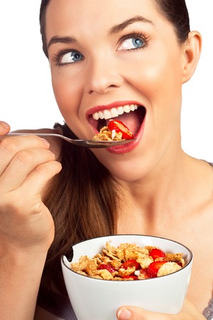 A close-up portrait of a beautiful young woman eating a healthy bowl of cereal with strawberries. Isolated over white.の写真素材