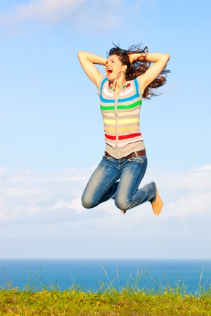 Beautiful young woman jumping up in the air laughing and holding her hair in front a of a great ocean viewの写真素材