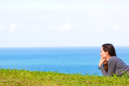 A sad and depressed young woman lying in the green grass looking sadly at  the oceanの写真素材