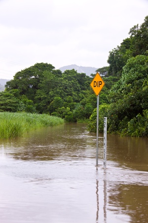 Flooded road with depth indicators and dip sign in Queensland, Australiaの写真素材