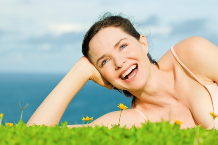 Beautiful young happy woman laying in green grass with yellow flowersの写真素材