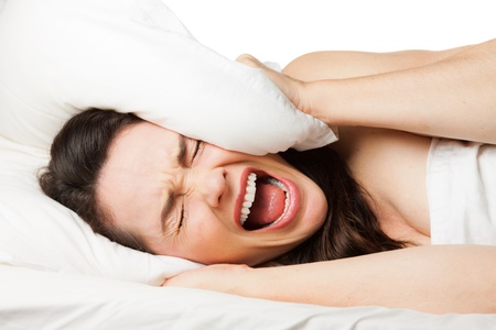 A frustrated tired woman hides her head in her pillow and screams beacuse she canの写真素材