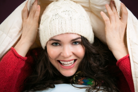 A beautiful happy young woman peeking out from underneath the blankets of her bedの写真素材