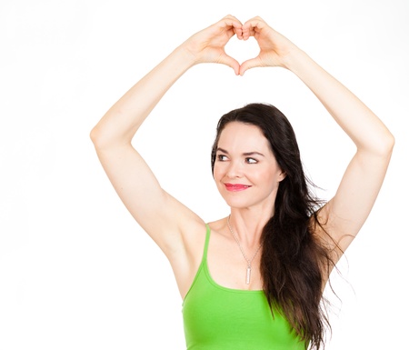 A beautiful young woman forming a love heart with her hands over her head and looks at copyspace. Isolated on whiteの写真素材