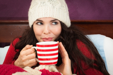 A beautiful young woman enjoying a hot frink under the blankets in bed.の写真素材