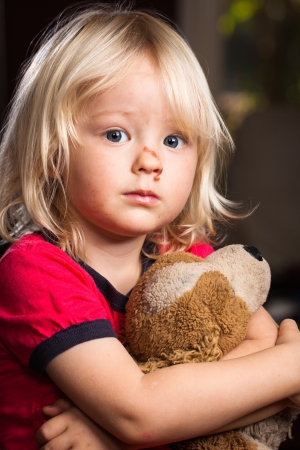 A sad cute injured boy holding a stuffed toy dog の写真素材