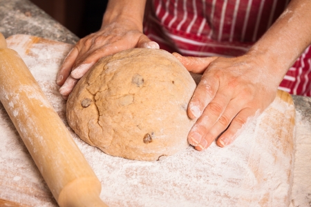 Close-up of hands on a bread dough with sultanas on a flour dusted chopping board の写真素材