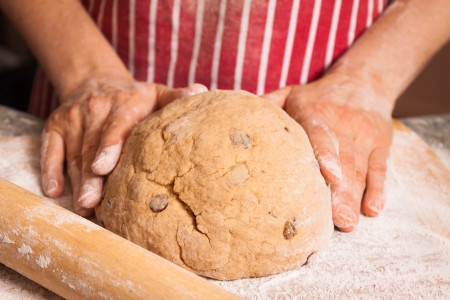 Close-up of hands kneeding a bread dough with sultanas on a flour dusted chopping board の写真素材