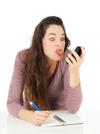 An annoyed woman is sticking her tongue out at her mobile phone  Isolated on white の写真素材