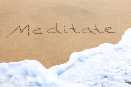 Meditate - written in the sand with a foamy wave underneathの写真素材