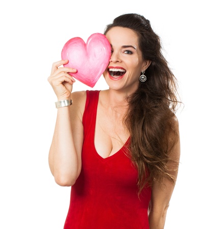 A happy laughing woman holding a red love heart in front of one eye  Isolated on white の写真素材