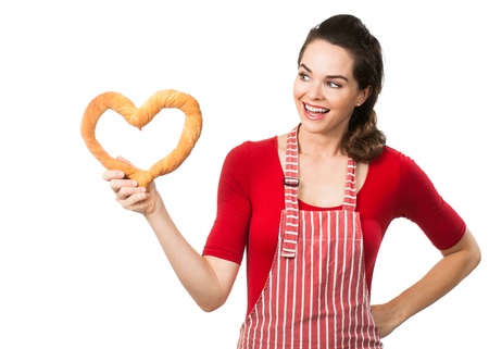 A beautiful woman wearing an apron smiling and holding and looking at a love heart made out of bread  Isolated on white の写真素材