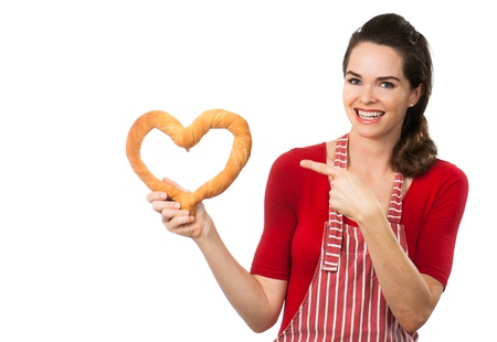 A beautiful woman wearing an apron smiling and pointing  at a love heart made out of bread  Isolated on white の写真素材