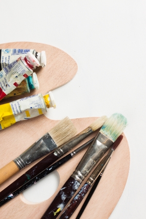 Paint brushes and tubes of paint on a palette on top of a blank canvasの写真素材