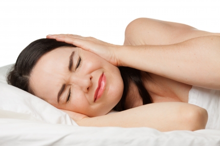 A sleepless woman lying in bed covering her ears. Isolated on white.の写真素材