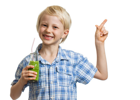 A cute young healthy boy holding green smoothie, smiling and pointing at copy-space  Isolated on white の写真素材