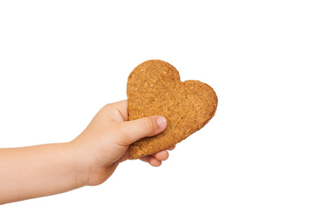 A child's hand is holding a love shaped gingerbread cookie. Isolated on white.の写真素材