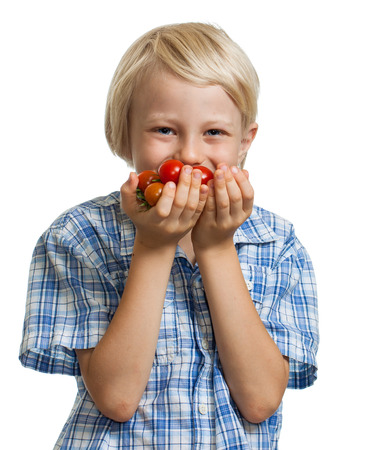 A cute happy blond boy smelling a bunch of vine ripened organic cherry tomatoes. Isolated on white.の写真素材