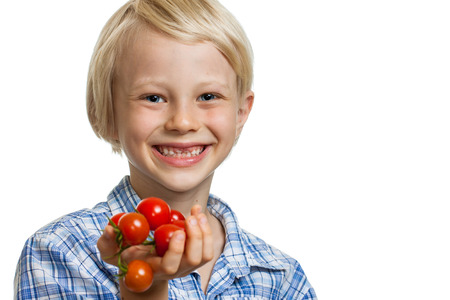 A cute happy blond boy holding a bunch of vine ripened organic cherry tomatoes. Isolated on white.の写真素材
