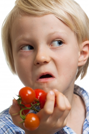 A funny boy holding a bunch of vine ripened organic cherry tomatoes and pulling a face. Isolated on white.の写真素材
