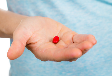Close-up shot of a hand holding a red pill.