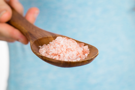 A hand holding a wooden spoon with Himalayan rock salt.の写真素材